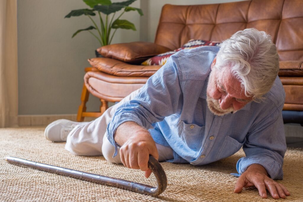 elder senior man lying floor after falling down with wooden walking stick beside couch rug living room home old man suffering with pain struggling get up after falling down home scaled